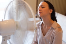 woman trying to stay cool in front of fan at home in summer